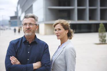 Businessman with arms crossed standing by businesswoman - JOSEF10145