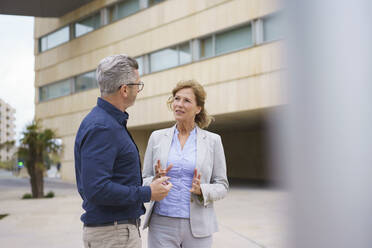 Businesswoman discussing with businessman in front of office building - JOSEF10157