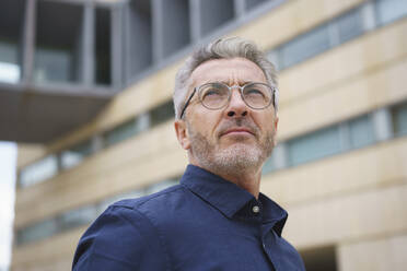 Businessman wearing eyeglasses in front of office building - JOSEF10169