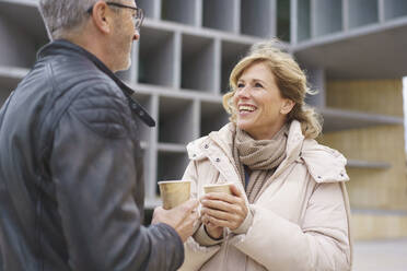 Happy woman and man holding disposable coffee cup standing in front of building - JOSEF10171