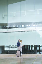 Geschäftsmann mit Koffer geht an einer Geschäftsfrau vor einer Glaswand vorbei - JOSEF10203