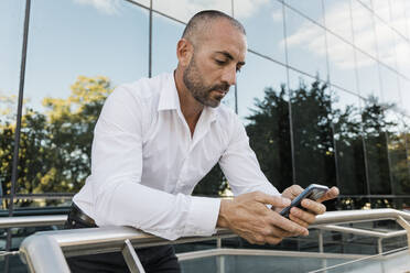 Mann benutzt Smartphone und lehnt sich an ein Geländer in der Nähe eines Gebäudes - JRVF02924