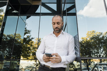 Mann, der ein Smartphone benutzt und sich gegen eine Glaswand lehnt - JRVF02925