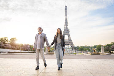 Glückliches reifes Paar, das sich an den Händen hält und vor dem Eiffelturm spazieren geht, Paris, Frankreich - OIPF01908