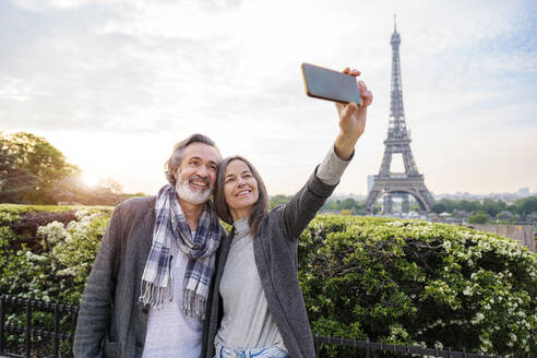 Glückliche Frau, die ein Selfie mit einem Mann durch ein Smartphone vor dem Eiffelturm macht, Paris, Frankreich - OIPF01911