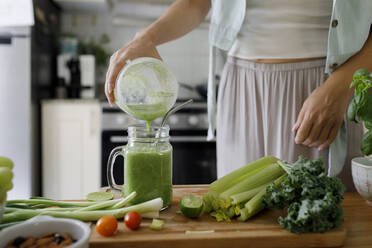 Hand einer Frau, die einen Smoothie aus einem Entsafter zu Hause in ein Einmachglas gießt - TYF00186