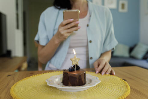 Frau fotografiert Geburtstagskuchen mit brennender Sternformkerze durch Handy - TYF00205