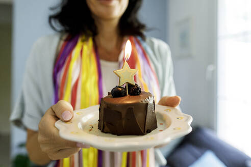 Hände einer Frau, die einen Geburtstagskuchen mit einer brennenden sternförmigen Kerze auf einem Teller zeigt - TYF00208