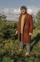 Lächelnder Mann mit Säge auf einer Baumfarm an einem sonnigen Tag - OGF01239