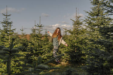 Happy girl with arms outstretched standing amidst fir tree farm - OGF01241