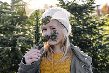 Mädchen hält Tannenzweig und zwinkert auf einer Weihnachtsbaumfarm - OGF01245