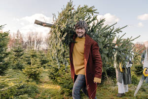 Man carrying Christmas tree on shoulder at farm - OGF01247