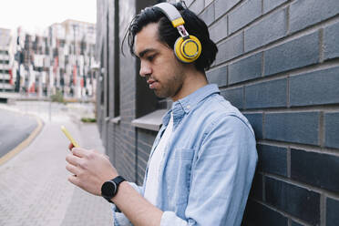 Mann mit Kopfhörern und Smartphone an der Wand - ASGF02311