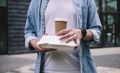 Man holding disposable cup and lunch box - ASGF02318