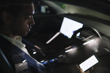 Businessman using smart phone sitting in electric car seen through window - ASGF02324