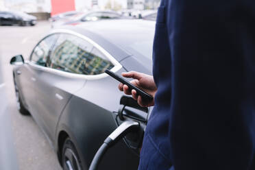 Geschäftsmann mit Smartphone an der Ladestation für Elektrofahrzeuge - ASGF02329