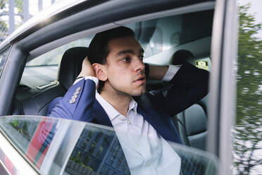Geschäftsmann mit Hand im Haar auf dem Rücksitz eines Elektroautos sitzend - ASGF02335