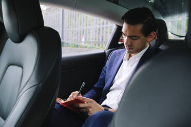 Geschäftsmann sitzt in einem Elektroauto und schreibt in sein Tagebuch - ASGF02337