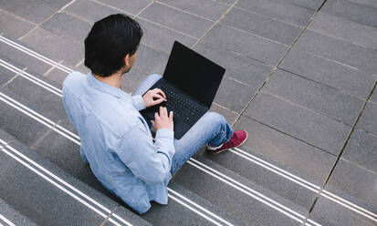 Man using laptop sitting on steps - ASGF02339