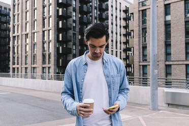 Mann mit Smartphone und Einwegbecher vor einem Gebäude stehend - ASGF02342
