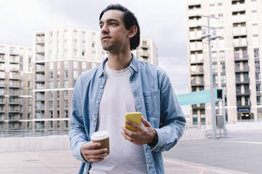 Man with smart phone holding disposable cup in city - ASGF02343