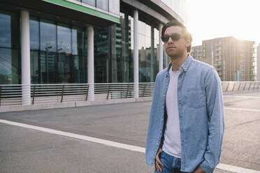 Man wearing sunglasses standing on road near building - ASGF02344