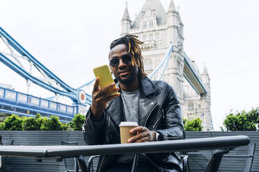 Man with sunglasses text messaging on smart phone, London, England - ASGF02353