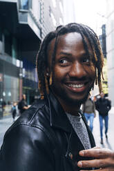 Smiling man with dreadlocks in city - ASGF02368