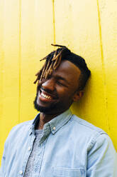 Junger Mann mit Dreadlocks lachend vor einer gelben Wand - ASGF02395