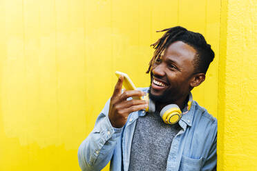 Happy man talking through speaker phone leaning on yellow wall - ASGF02397