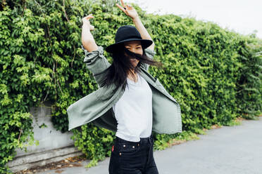 Happy woman with arms raised dancing in front of plants - MEUF05904