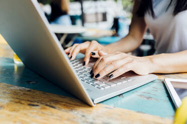 Hände eines selbstständigen Arbeiters tippen auf einem Laptop in einem Straßencafé - MEUF05932