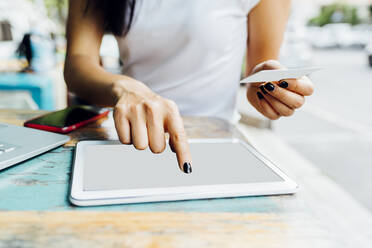 Hands of woman holding credit card making online payment through tablet PC at sidewalk cafe - MEUF05936