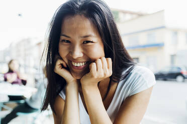 Happy young woman with head in hands sitting at sidewalk cafe - MEUF05939