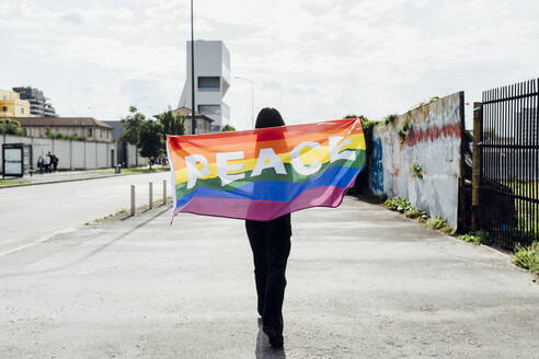 Eine junge Frau schwenkt eine Regenbogenfahne auf der Straße - MEUF05942