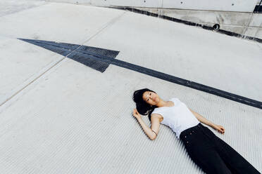 Young woman lying on driveway by arrow symbol - MEUF05966