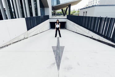 Young woman standing by arrow symbol at driveway - MEUF05968