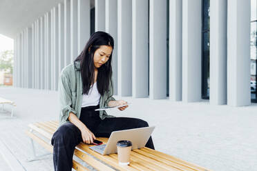 Junges Talent arbeitet flexibel und umweltbewusst mit Tablet und Laptop auf einer Bank im Freien - MEUF05972