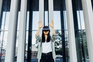 Young man wearing virtual reality simulator gesturing in front of column - MEUF05976