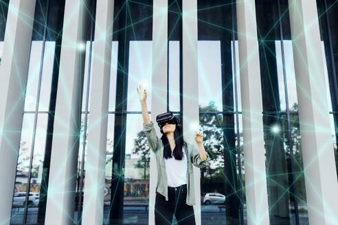 Woman wearing VR simulator with hand raised using transparent interface - MEUF05978