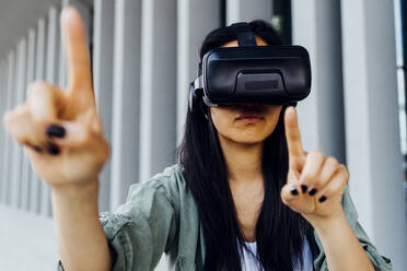 Eine junge Frau trägt einen VR-Simulator und zeigt auf etwas in der virtuellen Welt - MEUF05982