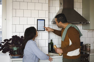 Mädchen schaut Vater an, der in der Küche zu Hause ein Hausautomatisierungsgerät benutzt - MASF30356