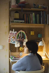 Rear view of thoughtful girl sitting at desk during studies at home - MASF30363