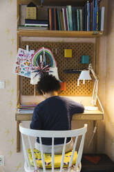 Rückansicht eines Jungen, der auf einem Stuhl am Schreibtisch sitzt, während er zu Hause lernt - MASF30367