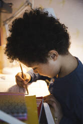 Boy with curly hair doing homework while writing in book - MASF30369