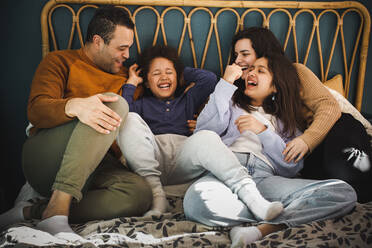 Glückliche Familie, die gemeinsam auf dem Bett sitzend zu Hause genießt - MASF30398