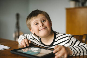 Portrait of happy boy with down syndrome sitting at table - MASF30400