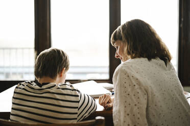 Rückansicht eines behinderten Sohnes, der bei seiner Mutter zu Hause lernt - MASF30404