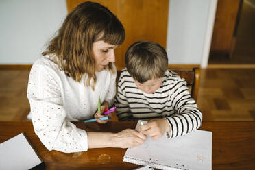 High angle view of mother teaching son with down syndrome to draw in book at table - MASF30406