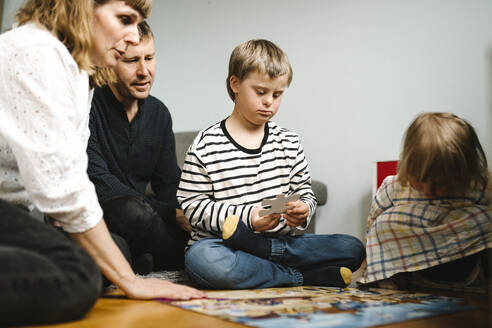Boy having disability joining jigsaw pieces sitting with family at home - MASF30417